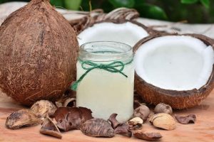 Coconut oil in a glass jar surrounded by fresh coconuts.