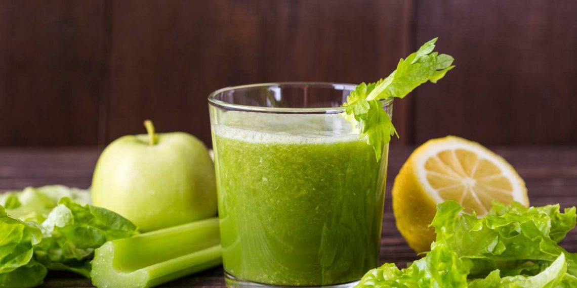 Green smoothie with celery, lettuce, apple, and lemon on wooden background.