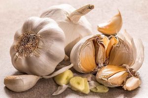 Garlic bulbs and cloves on a table with sliced pieces nearby.