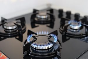 Gas stove burners with blue flames lit for cooking.