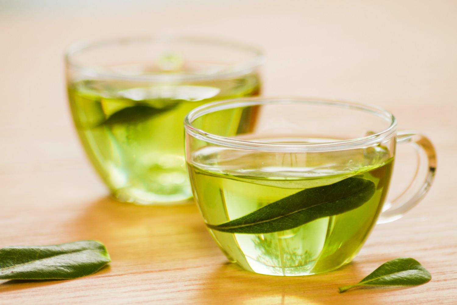 Two cups of fresh green tea with leaves on wooden table.