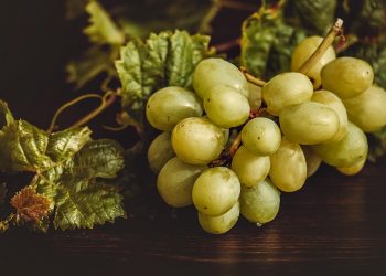 Green grapes with lush leaves on a wooden table.