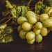Green grapes with lush leaves on a wooden table.