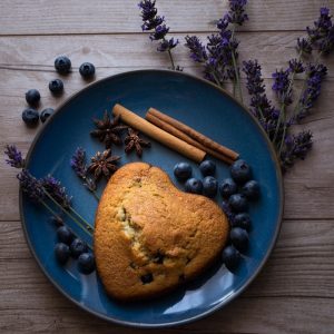 Heart-shaped blueberry scone on plate with spices and lavender.