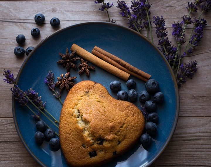 Heart-shaped blueberry scone on plate with spices and lavender.