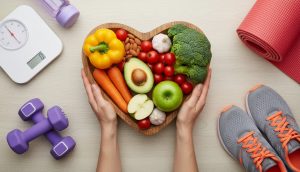 Healthy lifestyle essentials: vegetables, dumbbells, yoga mat, and scale on a table.