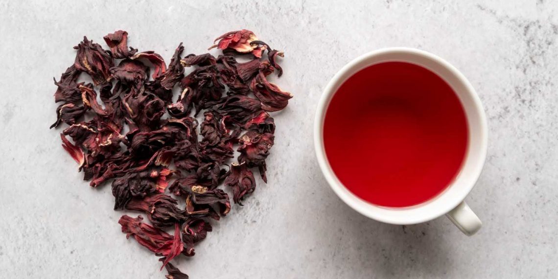 Dried hibiscus petals forming a heart next to a cup of hibiscus tea.
