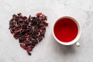 Dried hibiscus petals forming a heart next to a cup of hibiscus tea.