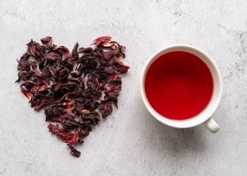 Dried hibiscus petals forming a heart next to a cup of hibiscus tea.