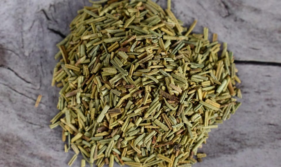 Dried rosemary leaves on rustic wooden surface.