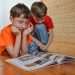 Two boys reading a book on a wooden floor.