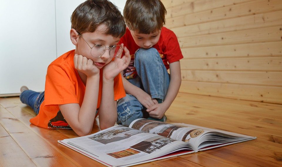 Two boys reading a book on a wooden floor.