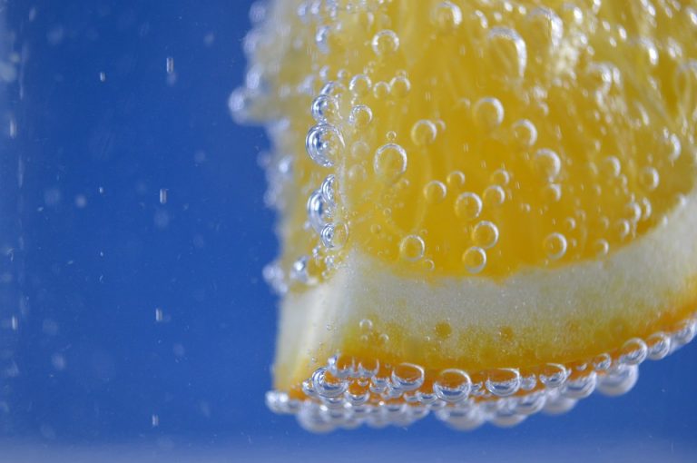 Orange slice with bubbles in water against blue background.