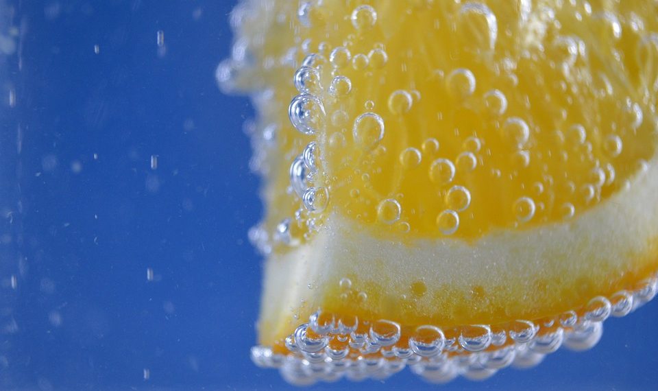 Orange slice with bubbles in water against blue background.