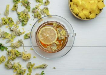Herbal tea with lemon slice and dried flowers on white table.