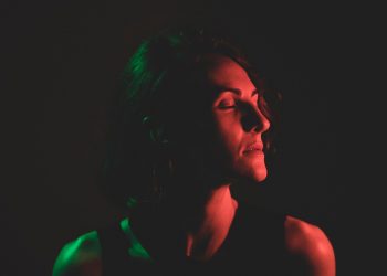 Person in dramatic red and green lighting with closed eyes.