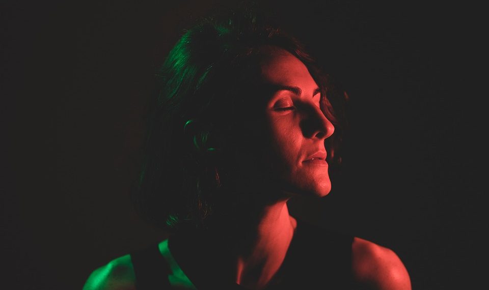 Person in dramatic red and green lighting with closed eyes.