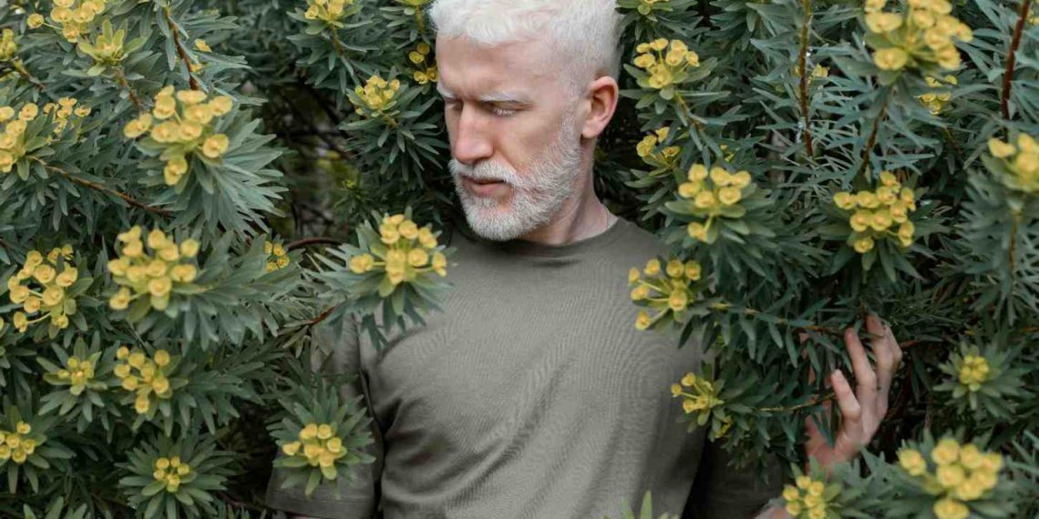Man standing among lush green plants with yellow flowers.