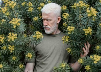 Man standing among lush green plants with yellow flowers.