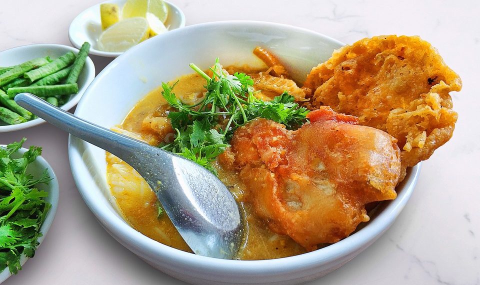 Bowl of spicy curry with fried snacks and fresh herbs.