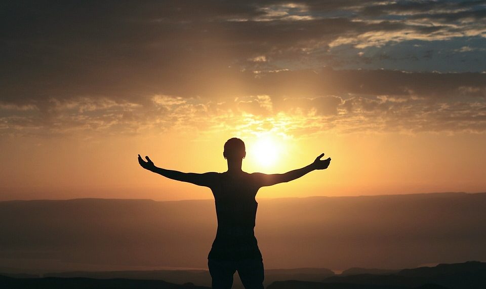 Person with outstretched arms embracing sunrise.