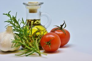 Garlic, rosemary, tomatoes, and olive oil arranged together.