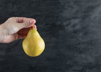 Hand holding a ripe pear against a dark background.
