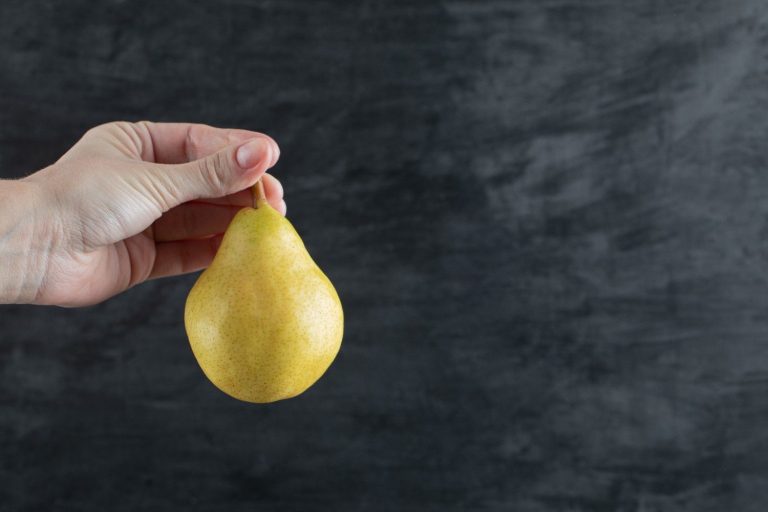 Hand holding a ripe pear against a dark background.