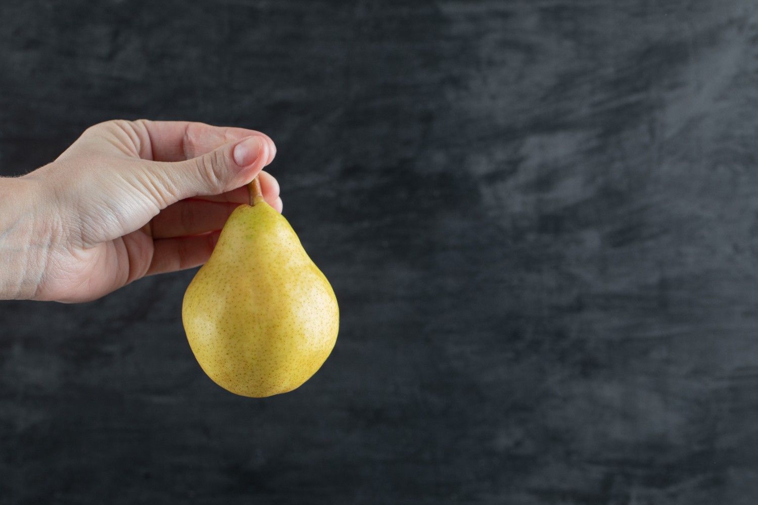 Hand holding a ripe pear against a dark background.