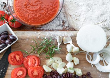 Tomato sauce and fresh pizza ingredients on wooden board.