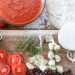 Tomato sauce and fresh pizza ingredients on wooden board.