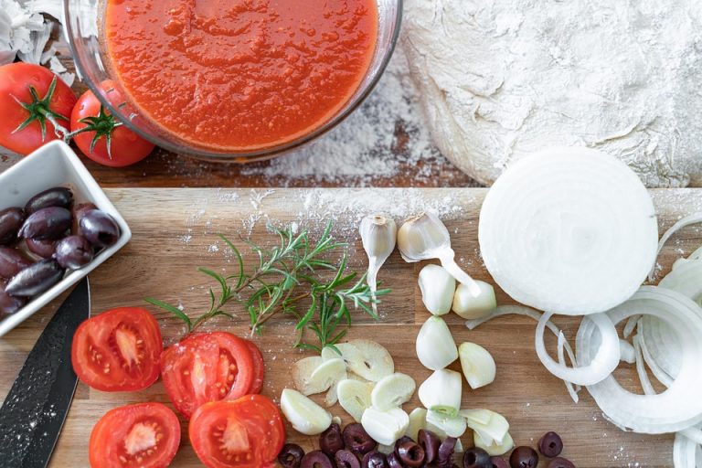 Tomato sauce and fresh pizza ingredients on wooden board.