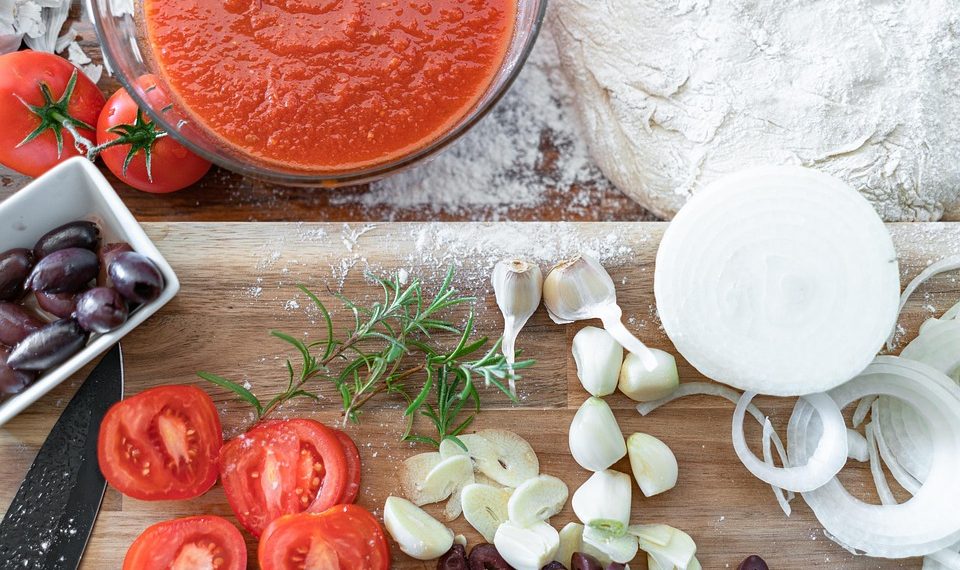 Tomato sauce and fresh pizza ingredients on wooden board.