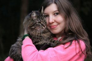 Woman embracing a tabby cat, smiling in a pink sweater.