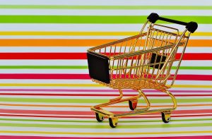 Golden miniature shopping cart on colorful striped background.