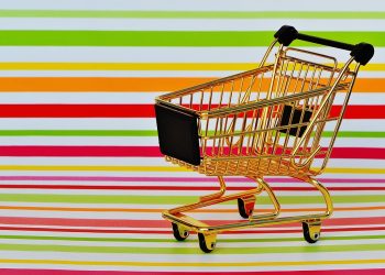 Golden miniature shopping cart on colorful striped background.