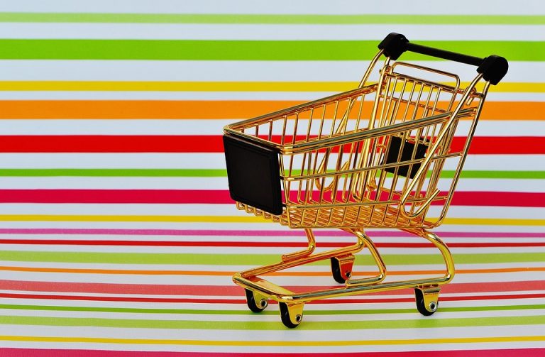 Golden miniature shopping cart on colorful striped background.