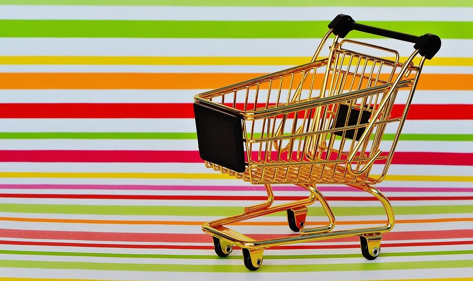 Golden miniature shopping cart on colorful striped background.