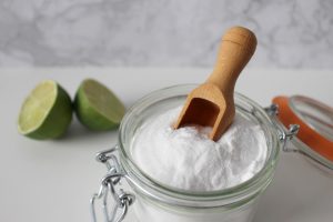 Baking soda in a glass jar with a wooden scoop, next to sliced lime.