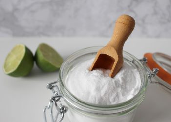 Baking soda in a glass jar with a wooden scoop, next to sliced lime.