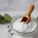 Baking soda in a glass jar with a wooden scoop, next to sliced lime.