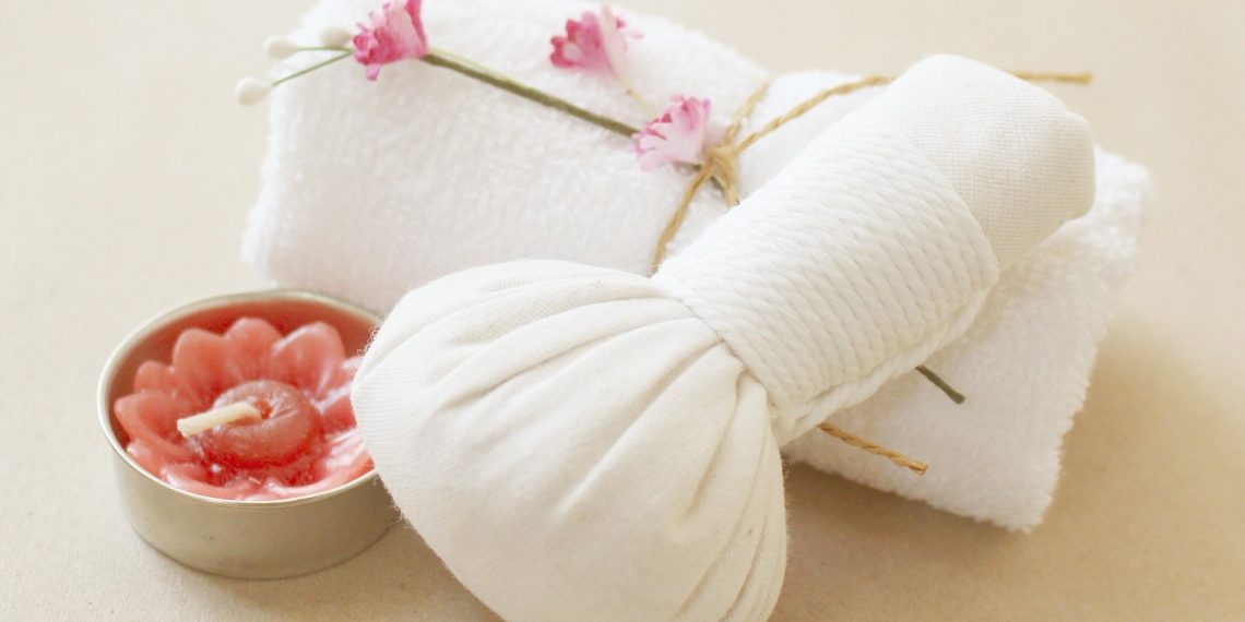 Spa towel and herbal compress with pink flower candle for relaxation.