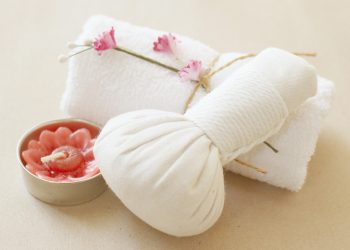 Spa towel and herbal compress with pink flower candle for relaxation.