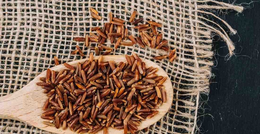 Red rice on a wooden spoon with burlap background.