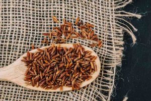 Red rice on a wooden spoon with burlap background.