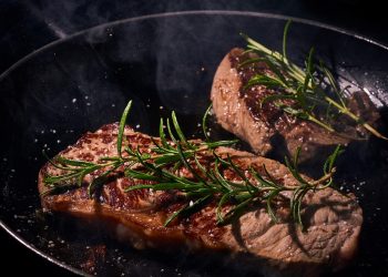 Grilled steak in a pan garnished with fresh rosemary.