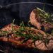 Grilled steak in a pan garnished with fresh rosemary.