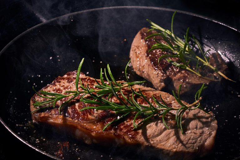 Grilled steak in a pan garnished with fresh rosemary.