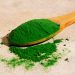 Green spirulina powder on a wooden spoon.