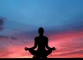 Silhouette meditating at sunset with vibrant sky.